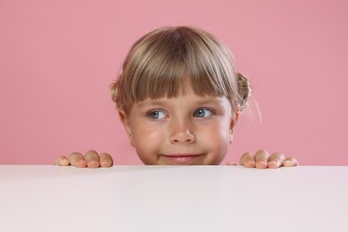 Photo of Curious little girl peeking over table against pink background