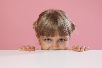 Photo of Curious little girl peeking over table against pink background