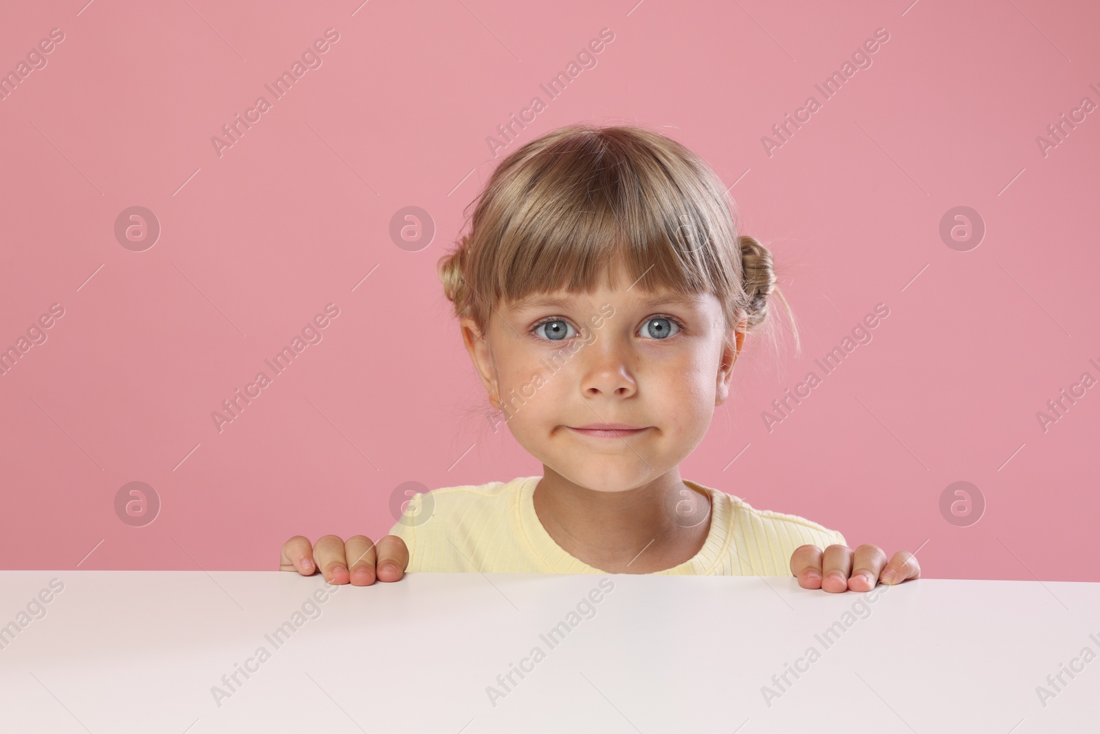 Photo of Curious little girl peeking over table against pink background