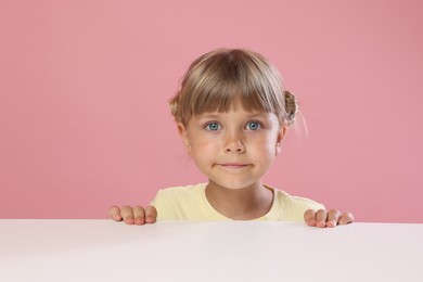 Photo of Curious little girl peeking over table against pink background