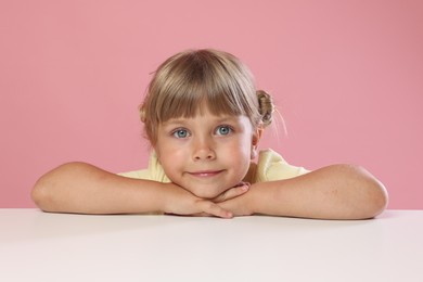 Photo of Curious little girl peeking over table against pink background