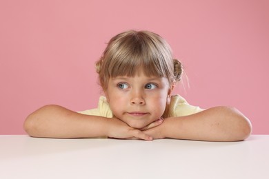 Photo of Curious little girl peeking over table against pink background