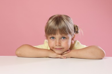 Photo of Curious little girl peeking over table against pink background