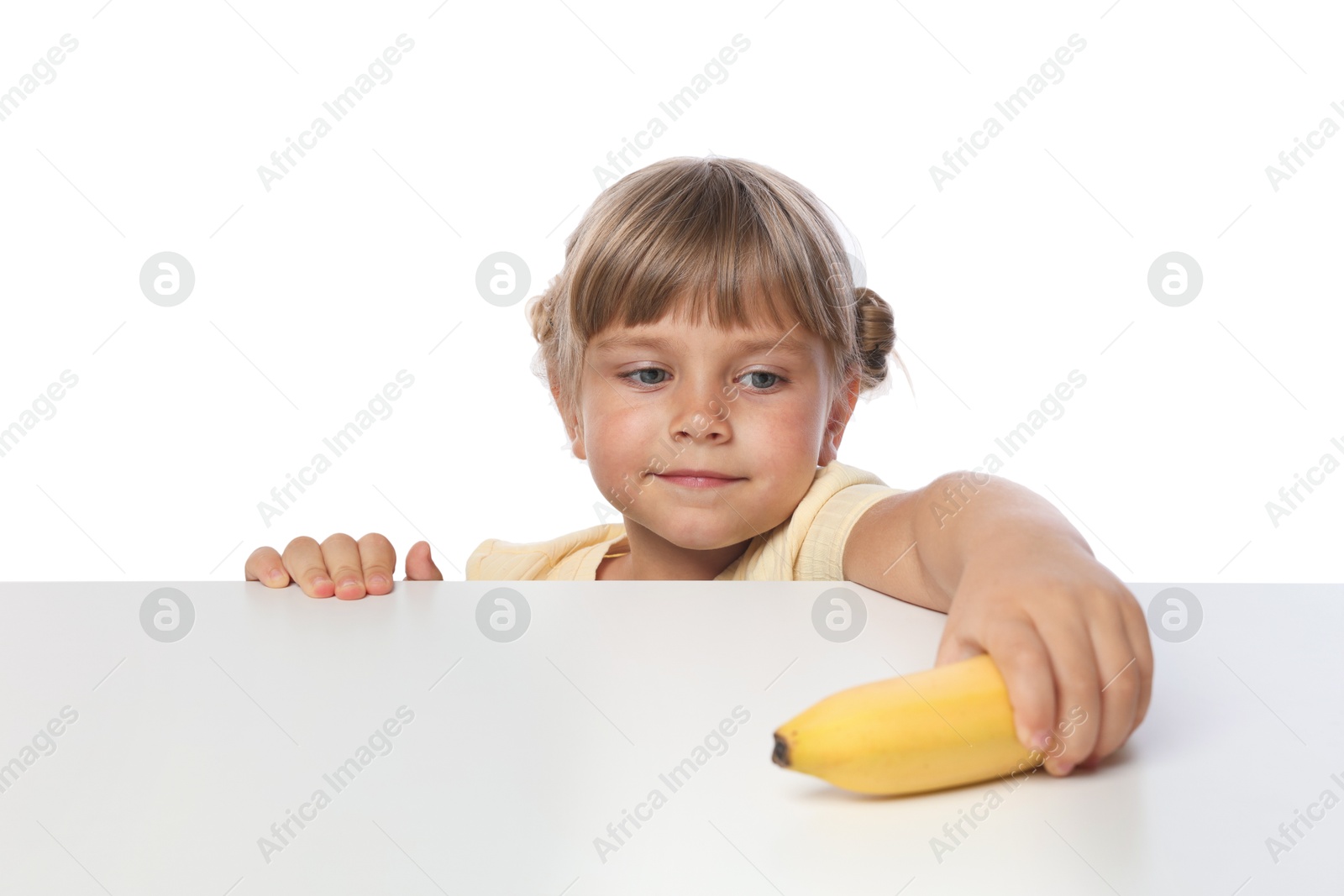 Photo of Cute little girl reaching for banana at table against white background