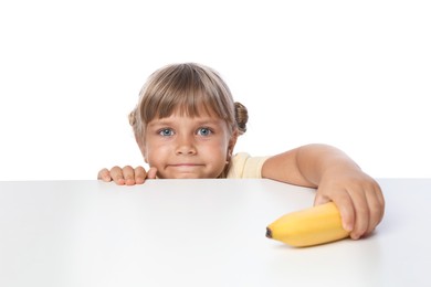 Photo of Cute little girl reaching for banana at table against white background