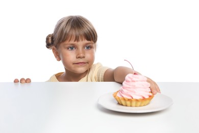 Photo of Cute little girl reaching for tasty dessert at table against white background