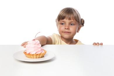 Photo of Cute little girl reaching for tasty dessert at table against white background