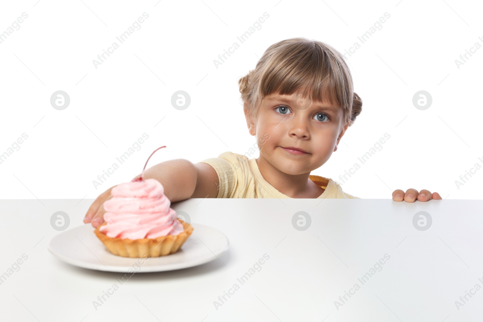 Photo of Cute little girl reaching for tasty dessert at table against white background