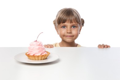 Photo of Cute little girl reaching for tasty dessert at table against white background