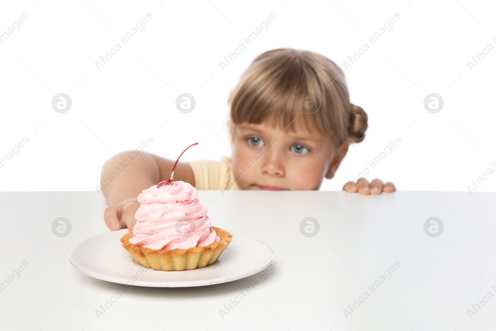 Photo of Cute little girl reaching for tasty dessert at table against white background