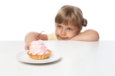 Photo of Cute little girl reaching for tasty dessert at table against white background