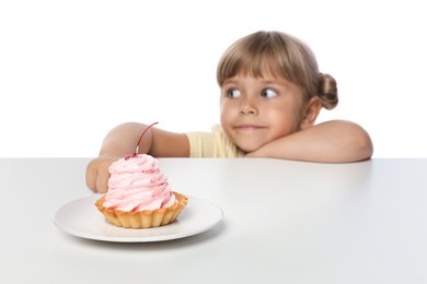Photo of Cute little girl reaching for tasty dessert at table against white background