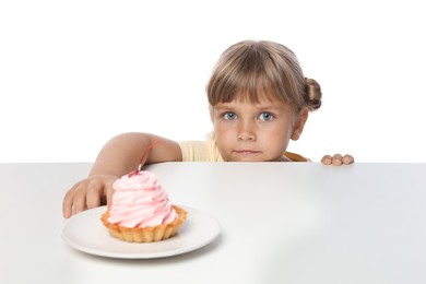 Photo of Cute little girl reaching for tasty dessert at table against white background
