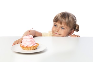 Photo of Cute little girl reaching for tasty dessert at table against white background