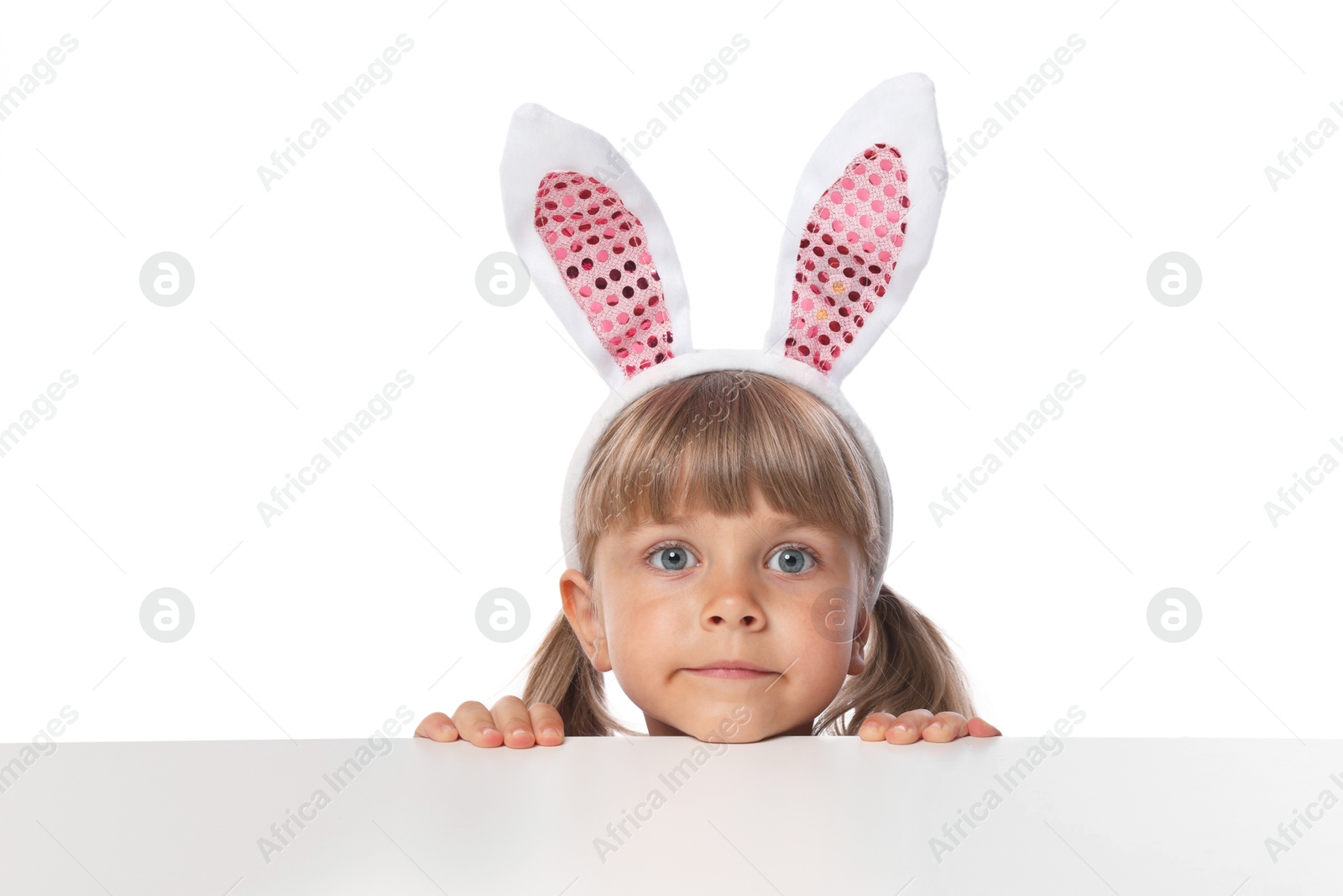 Photo of Curious little girl in bunny ears peeking over table against white background