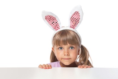 Photo of Curious little girl in bunny ears peeking over table against white background