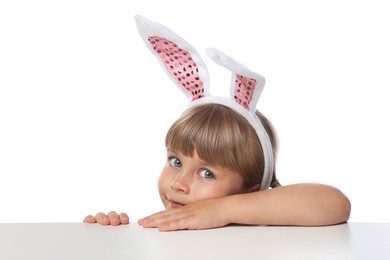 Photo of Curious little girl in bunny ears peeking over table against white background