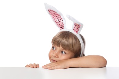 Photo of Curious little girl in bunny ears peeking over table against white background