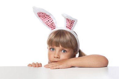 Photo of Curious little girl in bunny ears peeking over table against white background