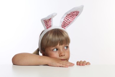 Photo of Curious little girl in bunny ears peeking over table against white background