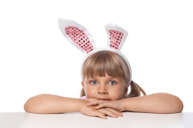 Photo of Curious little girl in bunny ears peeking over table against white background