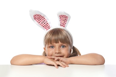 Photo of Curious little girl in bunny ears peeking over table against white background