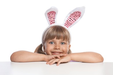 Photo of Curious little girl in bunny ears peeking over table against white background