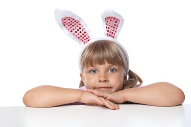Photo of Curious little girl in bunny ears peeking over table against white background