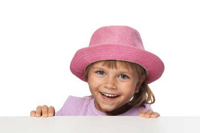 Photo of Curious little girl in pink hat peeking over table against white background