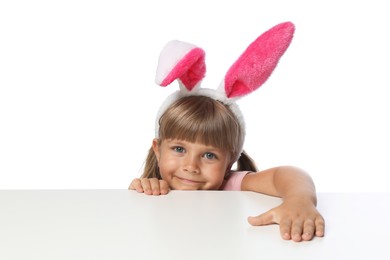 Photo of Curious little girl in bunny ears peeking over table against white background