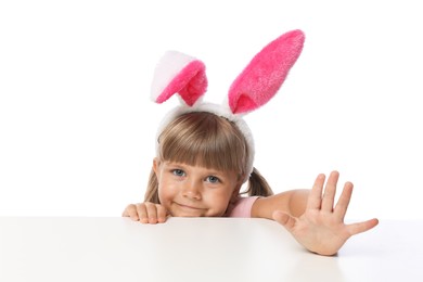 Photo of Curious little girl in bunny ears peeking over table against white background