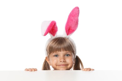 Photo of Curious little girl in bunny ears peeking over table against white background