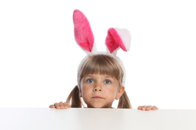 Photo of Curious little girl in bunny ears peeking over table against white background