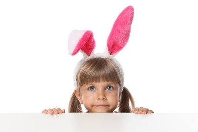 Photo of Curious little girl in bunny ears peeking over table against white background