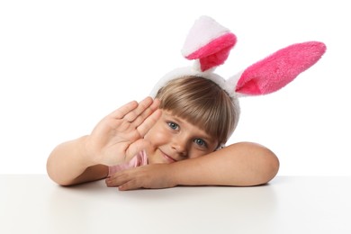 Photo of Curious little girl in bunny ears peeking over table against white background
