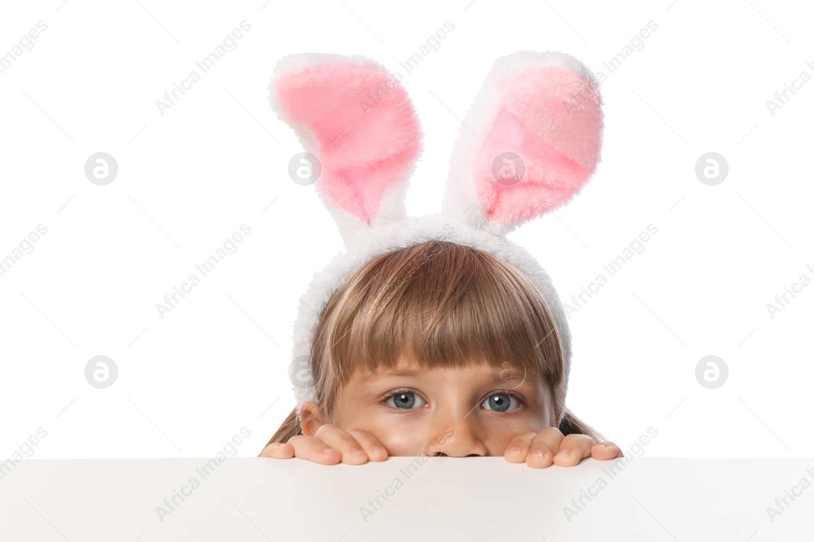 Curious little girl in bunny ears peeking over table against white background Photo of Curious little girl in bunny ears peeking over table against white background