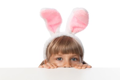 Photo of Curious little girl in bunny ears peeking over table against white background