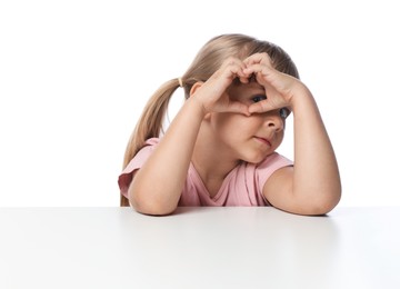 Photo of Cute little girl making heart gesture at table against white background