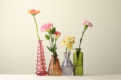 Photo of Different beautiful flowers in glass vases on white table against light grey background