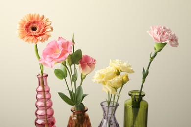 Photo of Different beautiful flowers in glass vases on light grey background, closeup