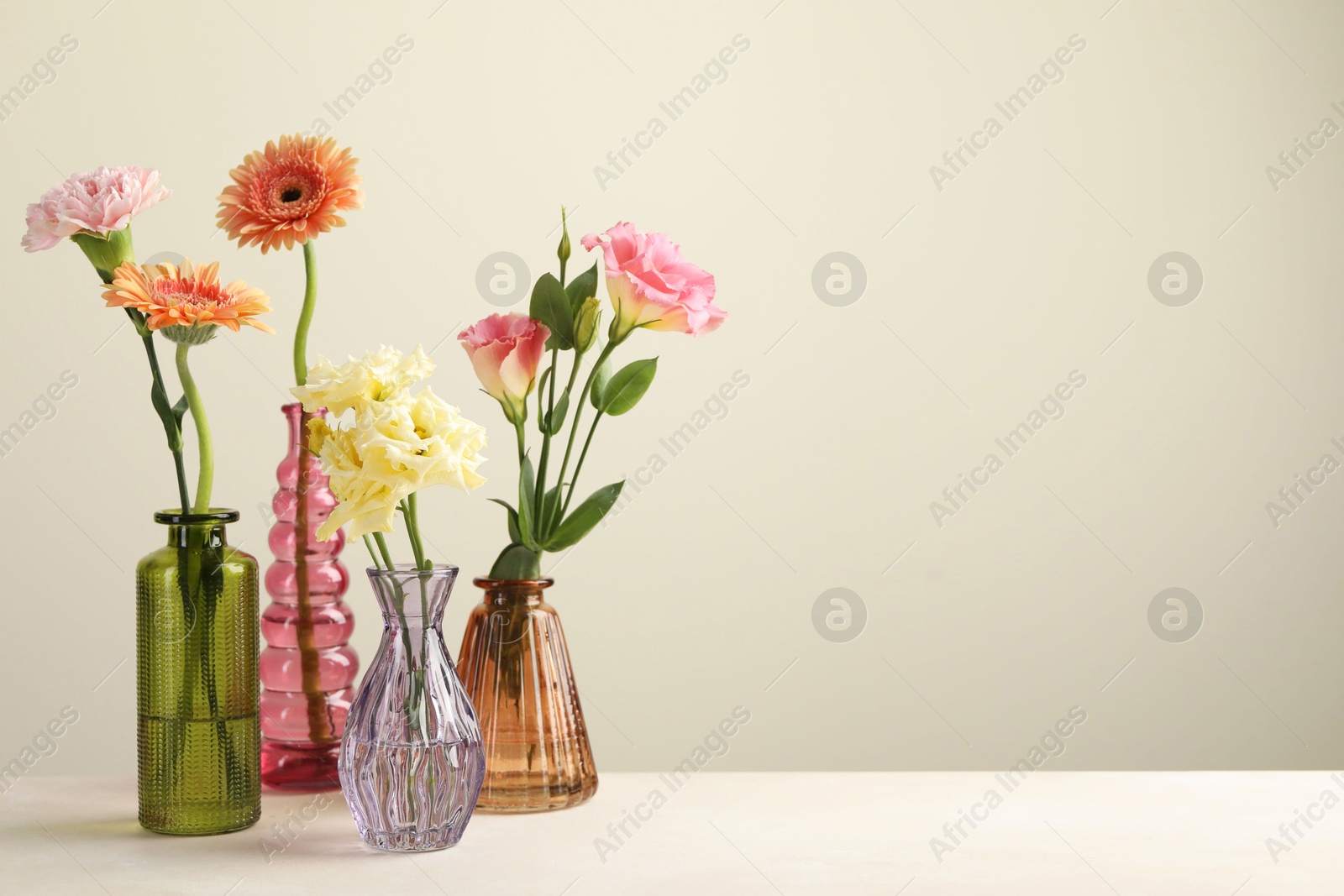 Different beautiful flowers in glass vases on white table against light grey background, space for text Photo of Different beautiful flowers in glass vases on white table against light grey background, space for text