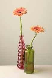 Photo of Beautiful gerbera flowers in glass vases on white table against light grey background