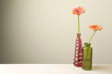 Photo of Beautiful gerbera flowers in glass vases on white table against light grey background, space for text