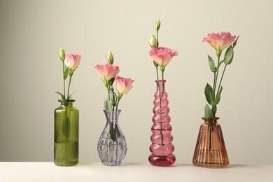 Photo of Beautiful eustoma flowers in glass vases on white table against light grey background