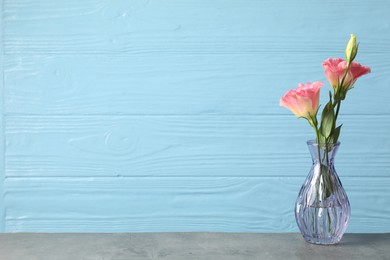 Photo of Beautiful eustoma flowers in glass vase on grey table against light blue wooden background, space for text