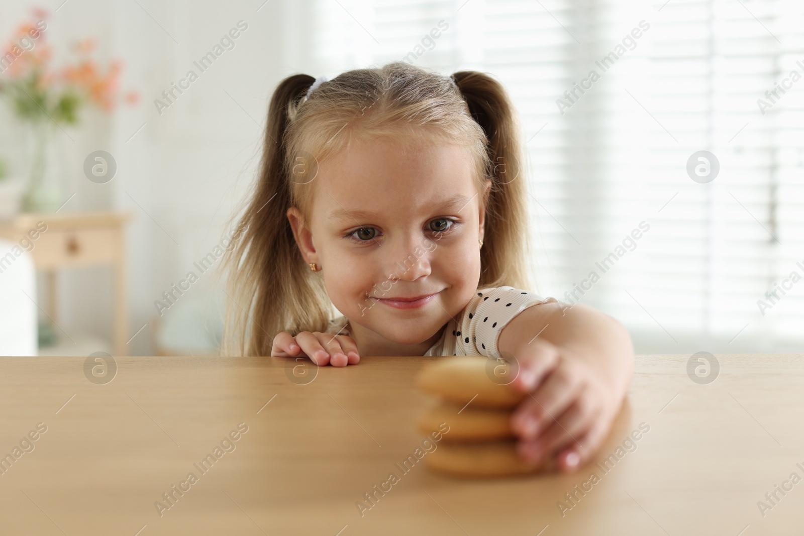 Photo of Cute little girl reaching for tasty cookies at wooden table indoors