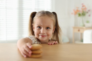 Photo of Cute little girl reaching for tasty cookies at wooden table indoors
