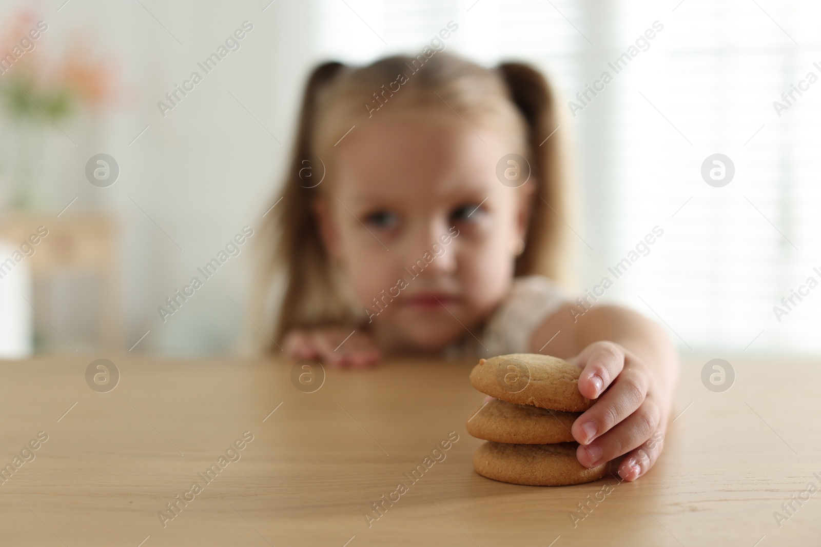 Photo of Cute little girl reaching for tasty cookies at wooden table indoors, selective focus