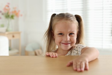 Photo of Curious little girl peeking over wooden table indoors, space for text