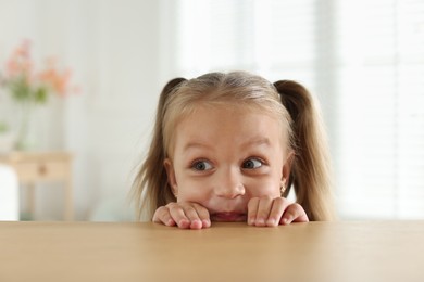 Photo of Curious little girl peeking over wooden table indoors